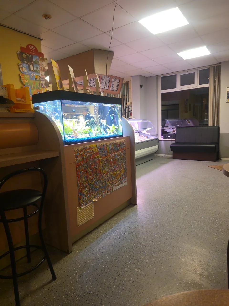 Binnen: zitbank, krukken en het aquarium bij de toonbank – Friture 't Pleintje